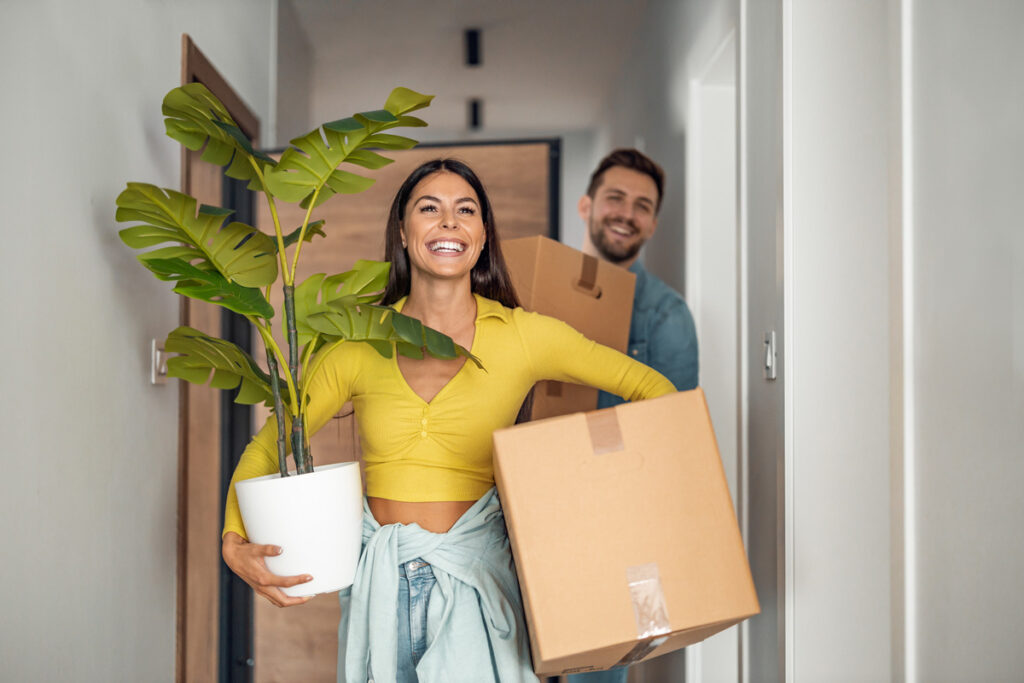 A smiling man and woman carrying items into their new affordable home in El Paso.